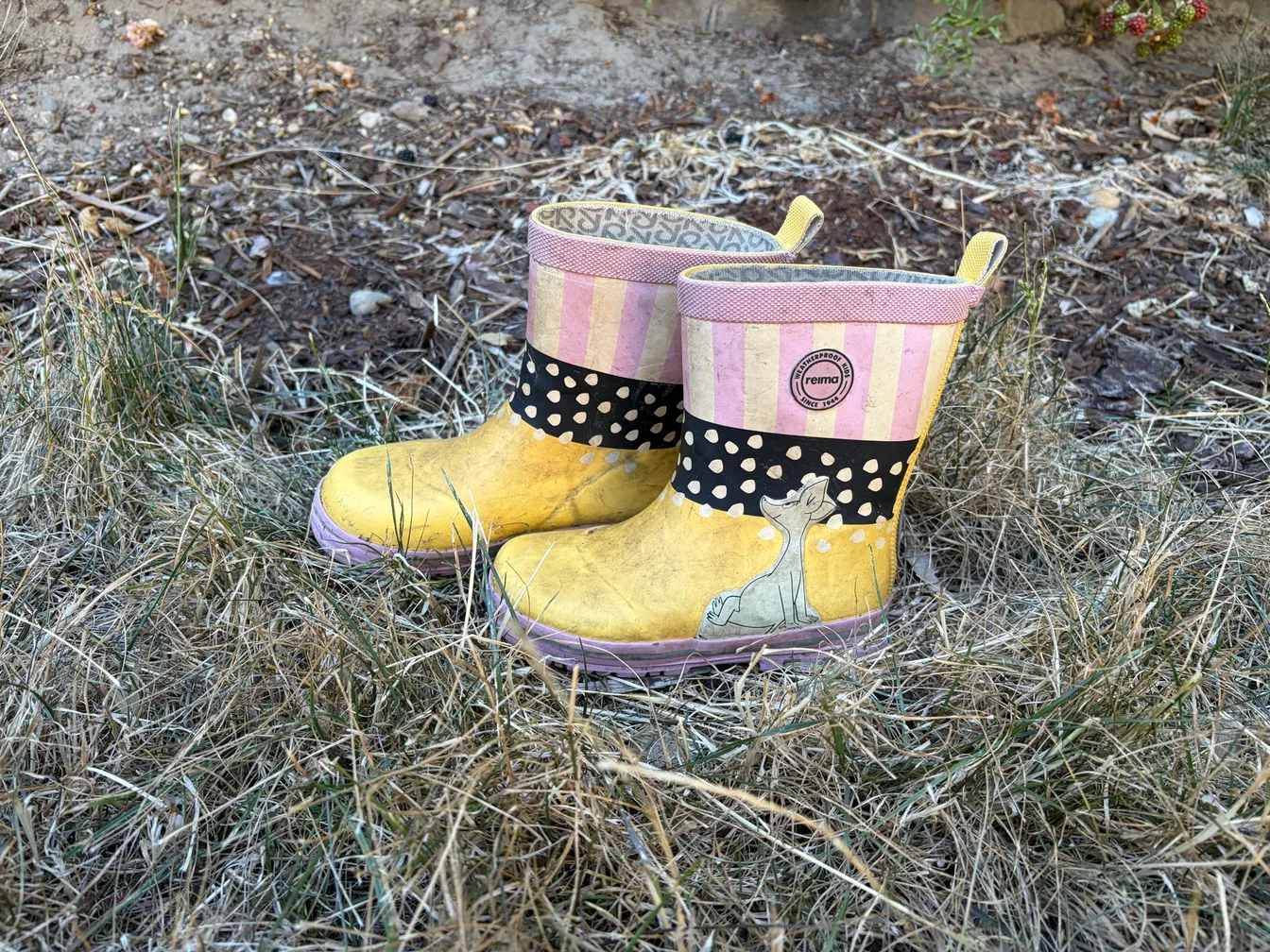 A pair of well-worn toddler Reima rain boots sitting in dry grass at a campsite